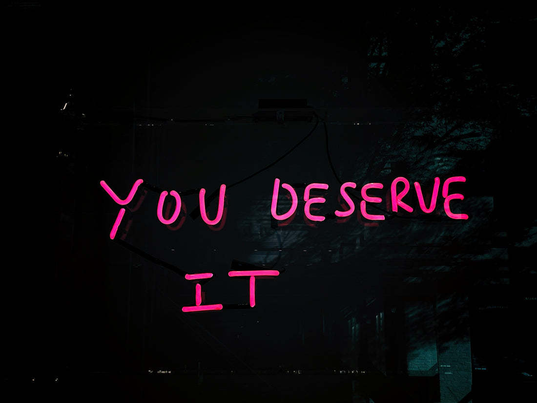 Bold neon sign reading “You Deserve It” glowing against a chic backdrop—radiating confidence and self-love. A true Unapologetically You vibe.